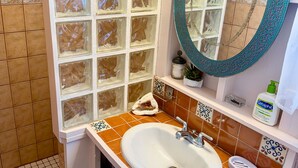 Ein Badezimmer mit einem weißen Waschbecken, einem Spiegel und einem Fenster mit dekorativen Glasscheiben.