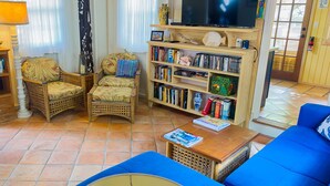 Ein Wohnzimmer mit einer Couch, zwei Sesseln, einem Couchtisch, einem Bücherregal und einem Fernseher.