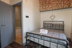 A bedroom with a metal bed frame, a grey checkered bedspread, a heart-shaped wall decoration, and a door leading to a bathroom. - Shoreline Studio Room No.2 (Newquay)