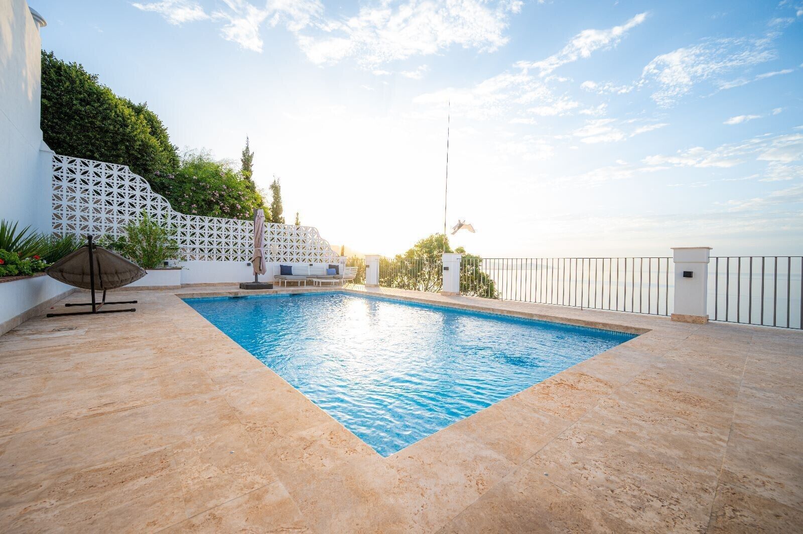 A swimming pool with a white fence, lounge chairs, and a pergola.