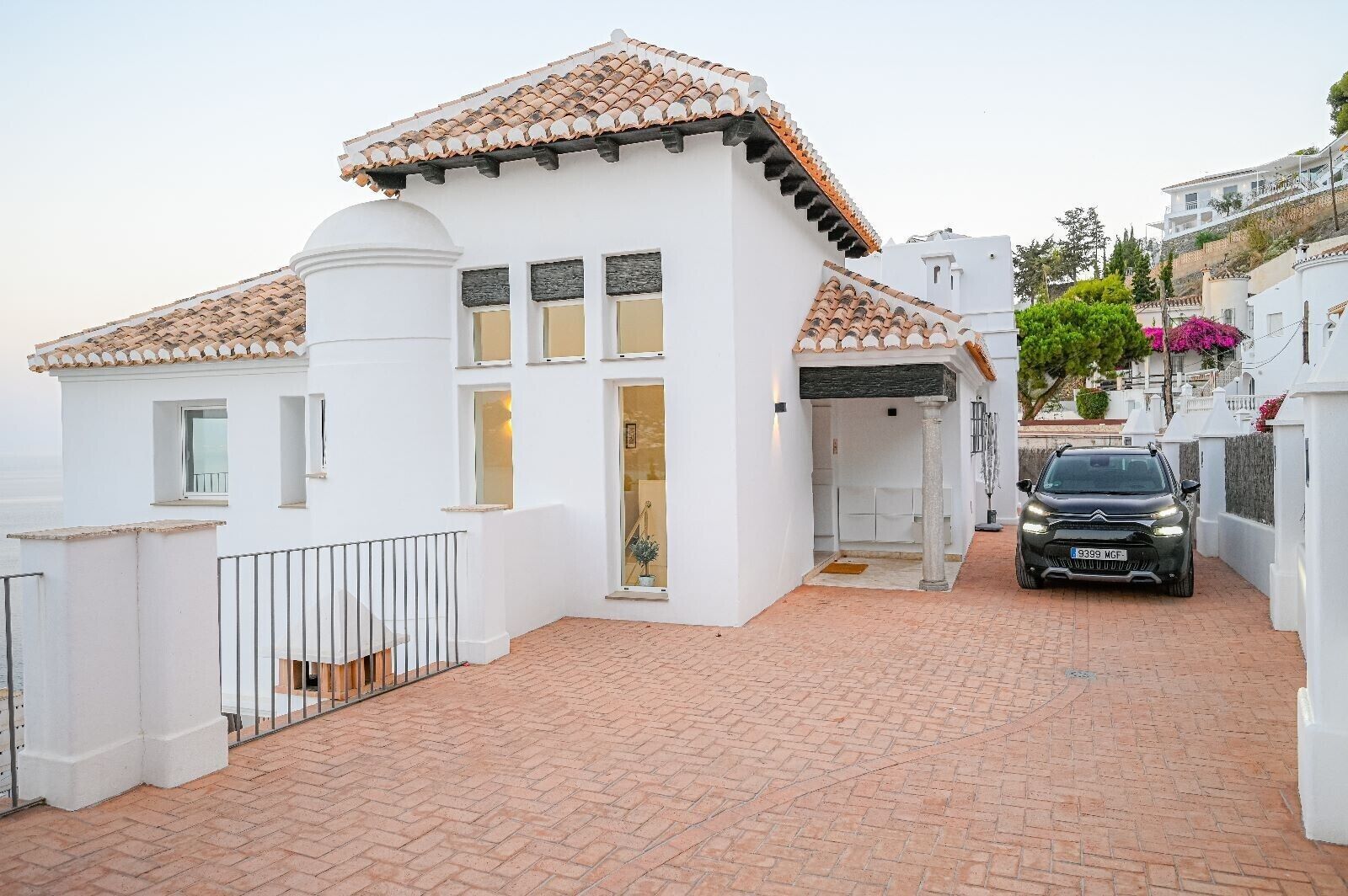 A white building with a tiled roof, a paved driveway, and a parked car.