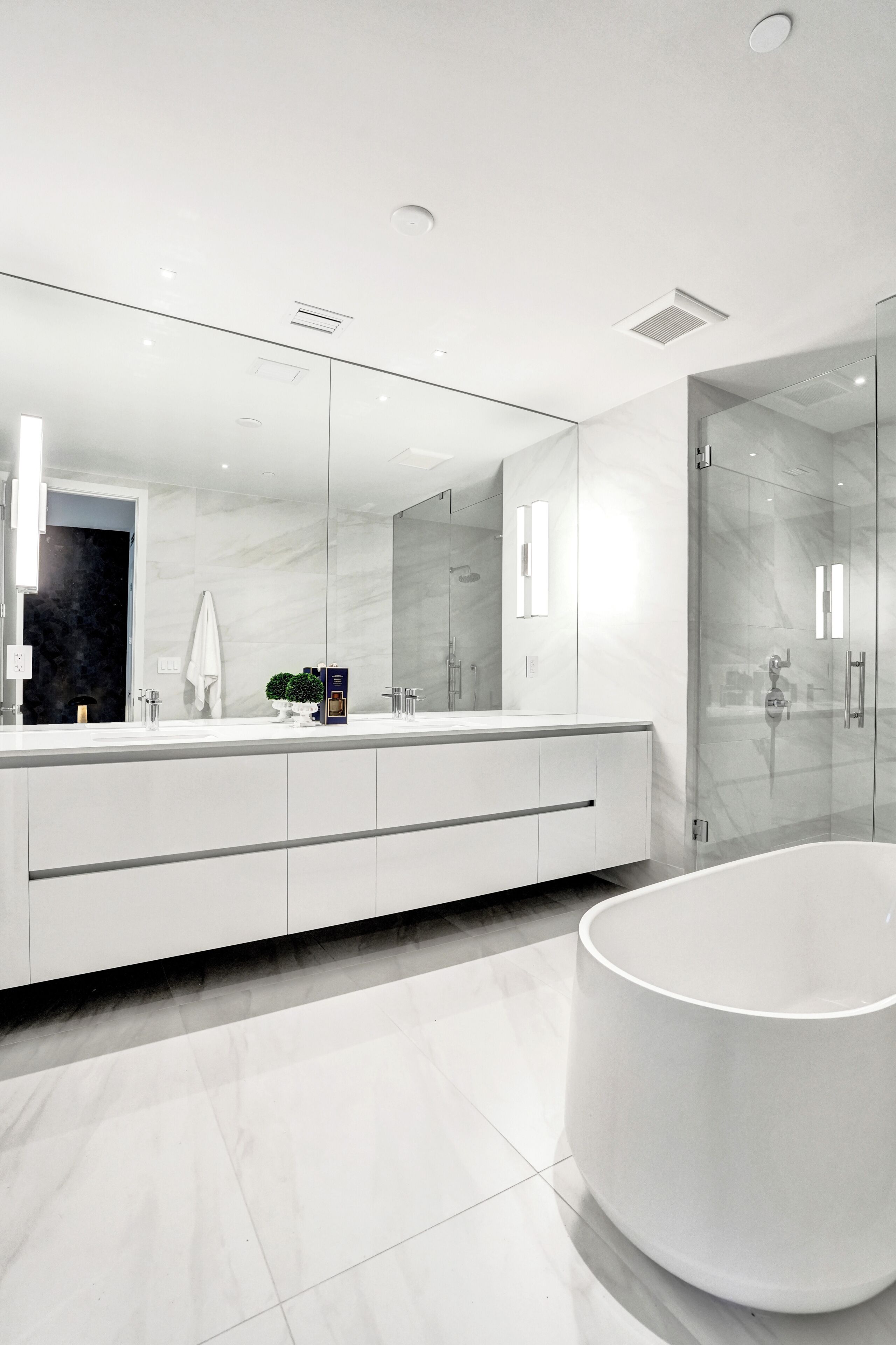 A modern bathroom with a large mirror, a white bathtub, and a glass-enclosed shower area.