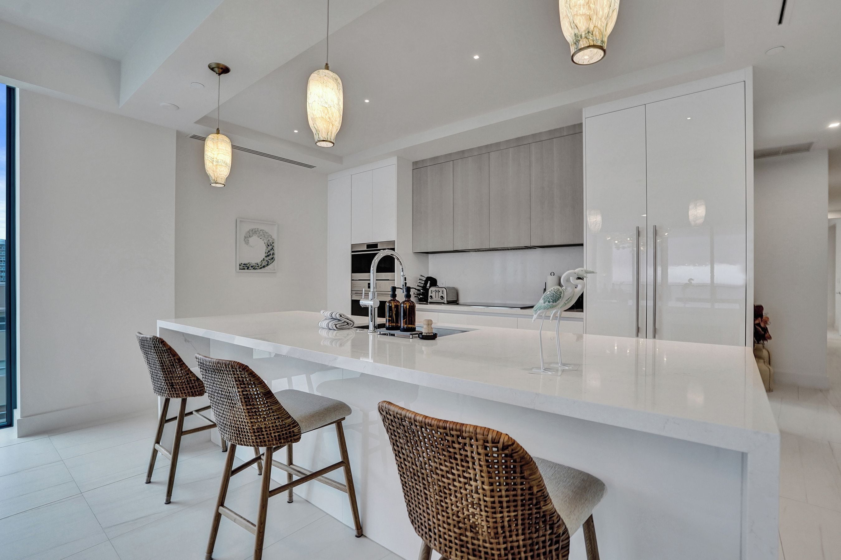 Una cocina moderna con una isla central, taburetes de bar, iluminación colgante y vistas a la ciudad.