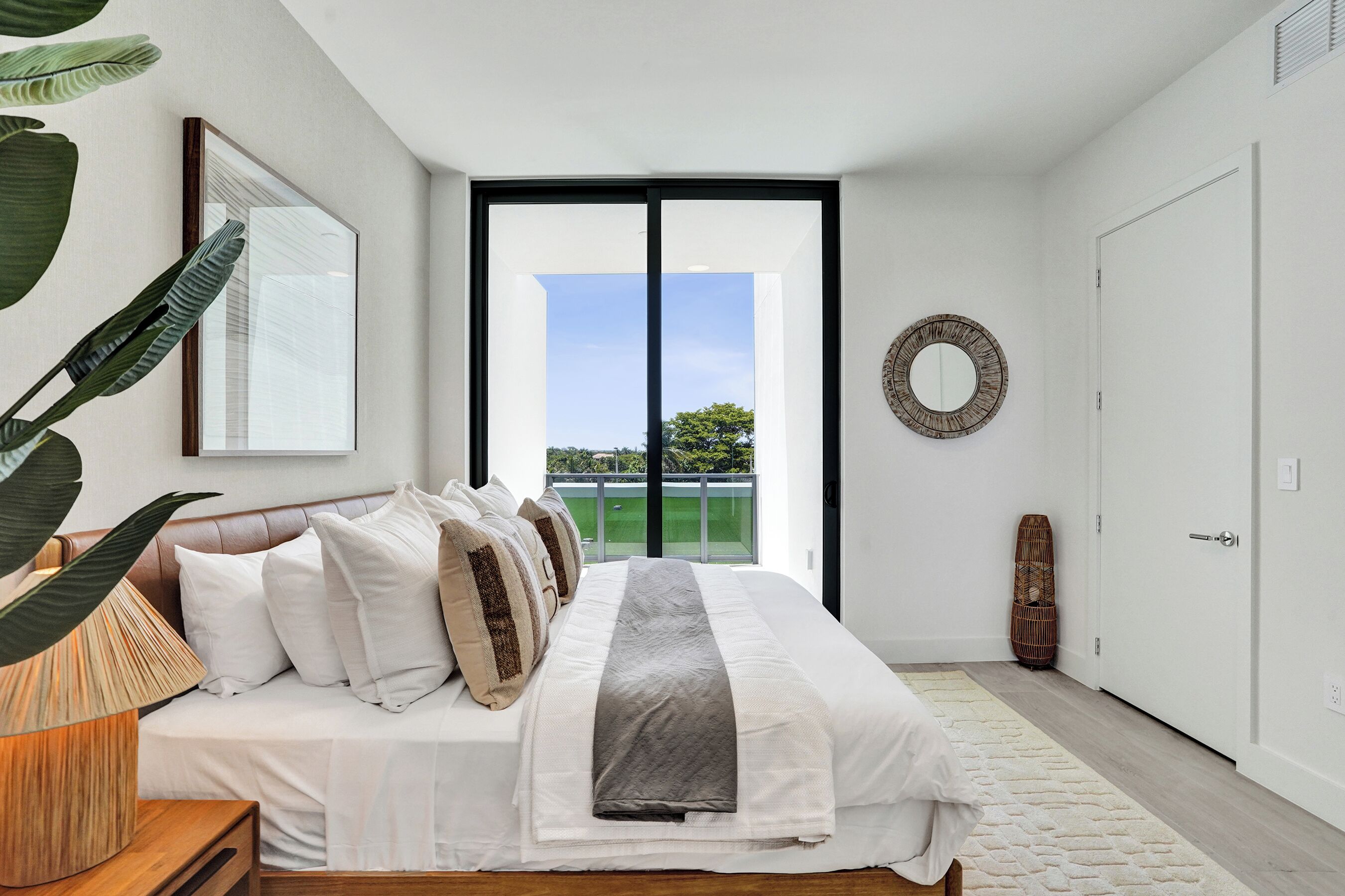 A modern bedroom with a large bed, a view of greenery outside, and a minimalist design.