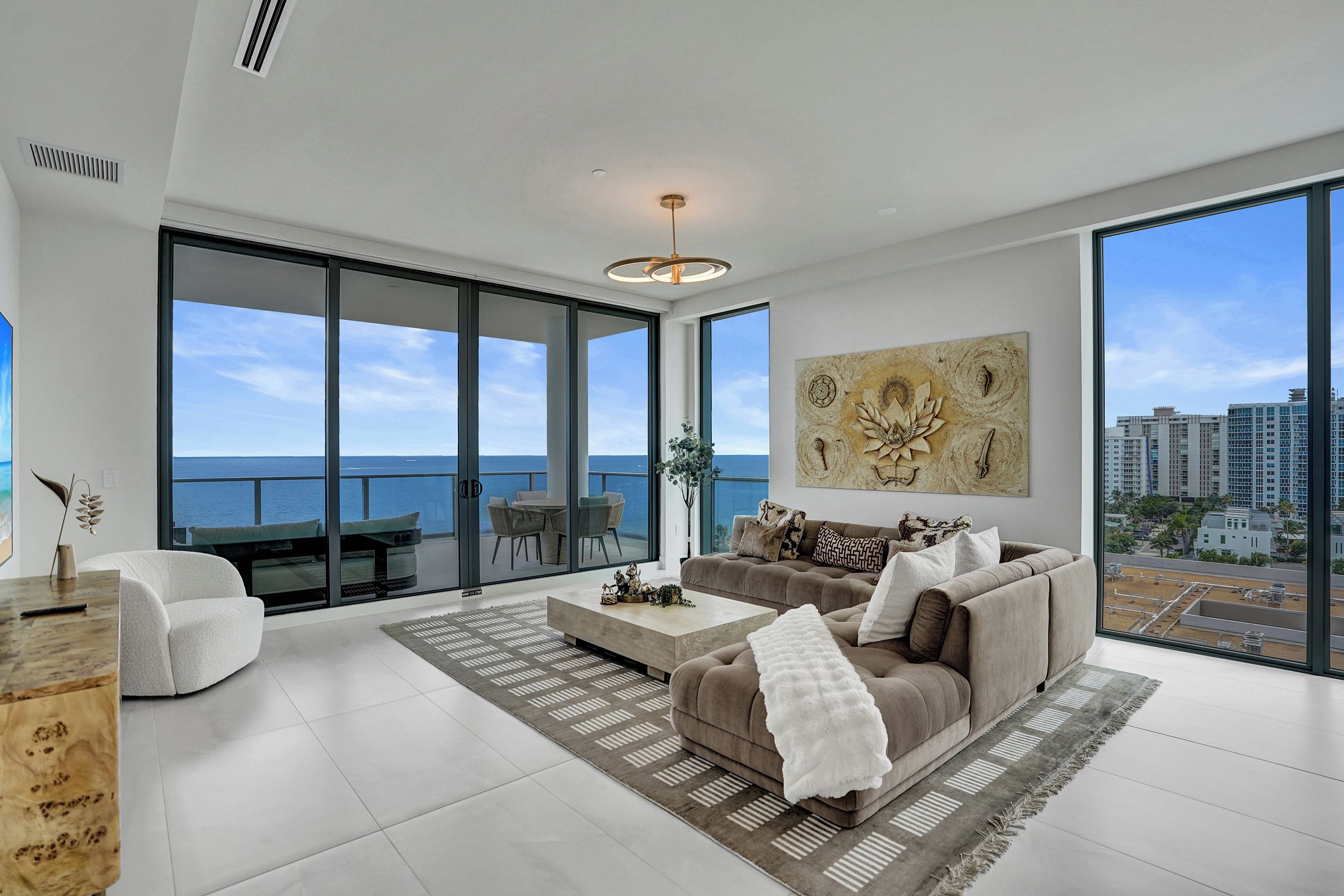 A modern living room with a large window overlooking the sea, a sofa, a coffee table, and a decorative wall piece.