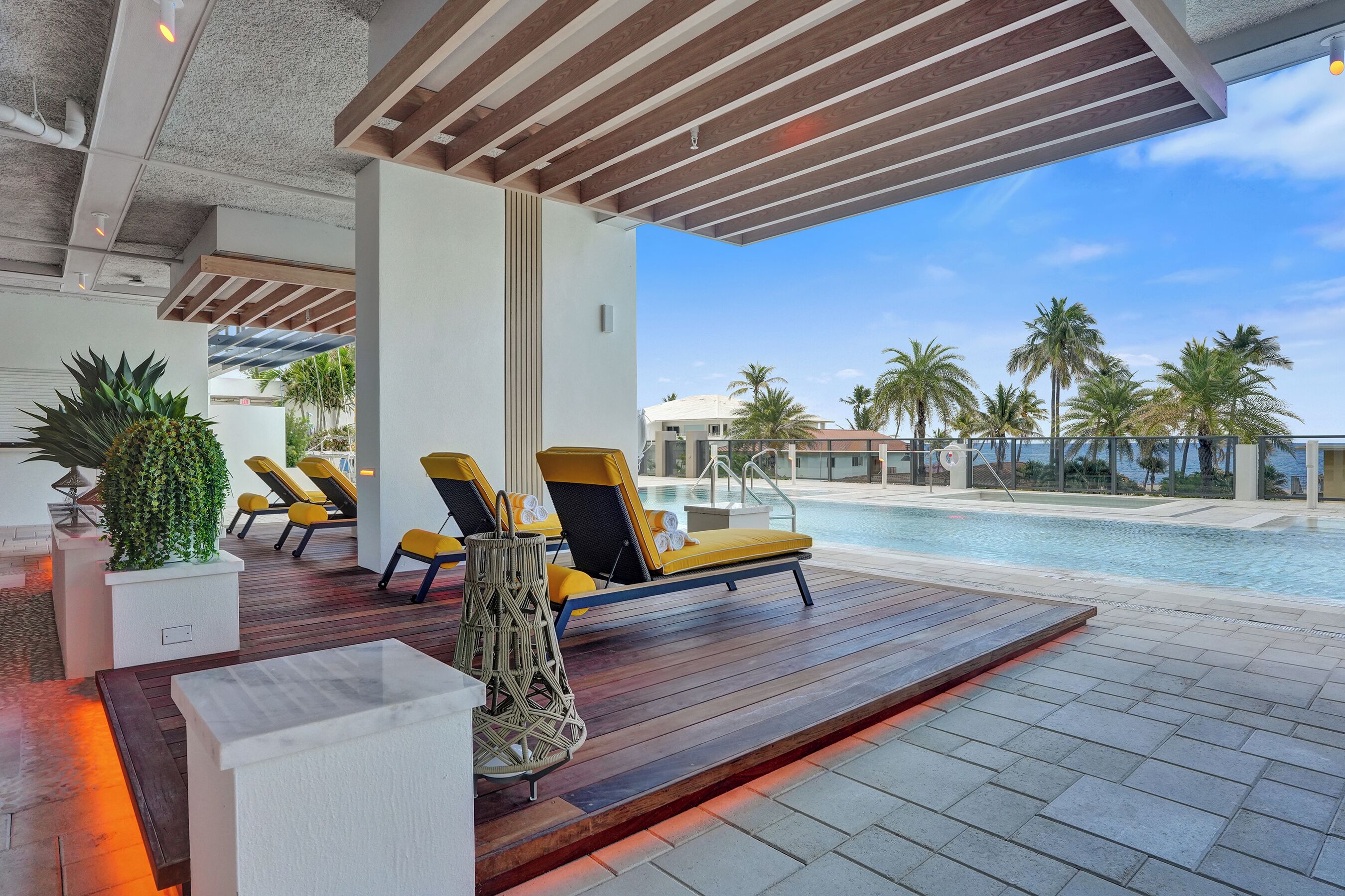 A poolside area with lounge chairs, a wooden deck, and a view of the ocean.
