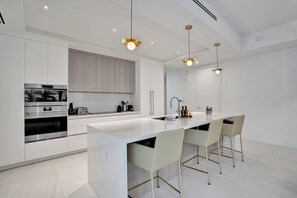 A modern kitchen with white cabinetry, a central island with bar stools, and pendant lighting. - Salato (Pompano Beach)