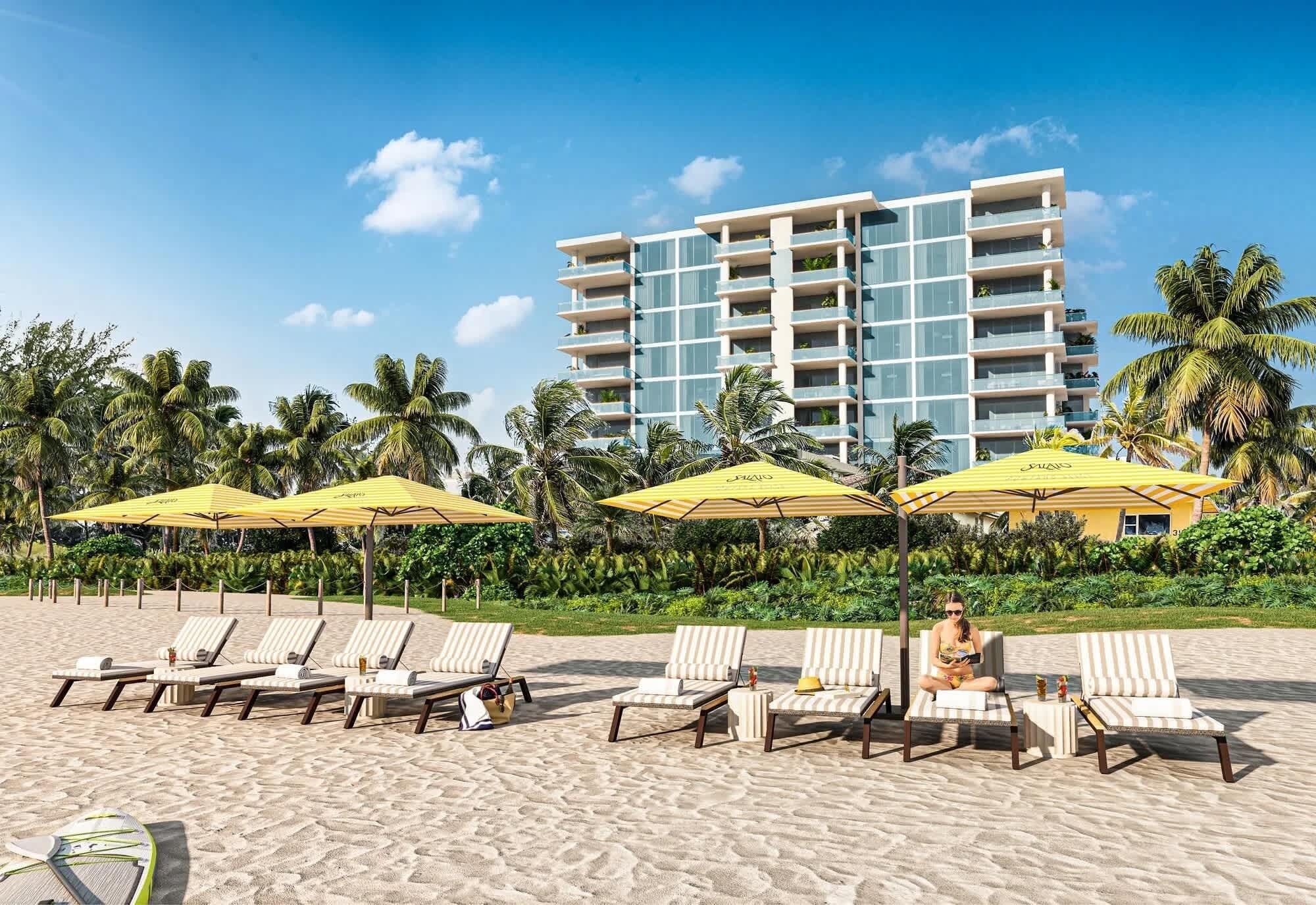 Ein Strand mit Liegestühlen und Sonnenschirmen, ein Hotel im Hintergrund und Palmen.