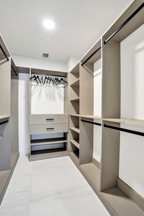A walk-in closet with open shelving, a hanging rod, and a built-in drawer unit. - Salato (Pompano Beach)