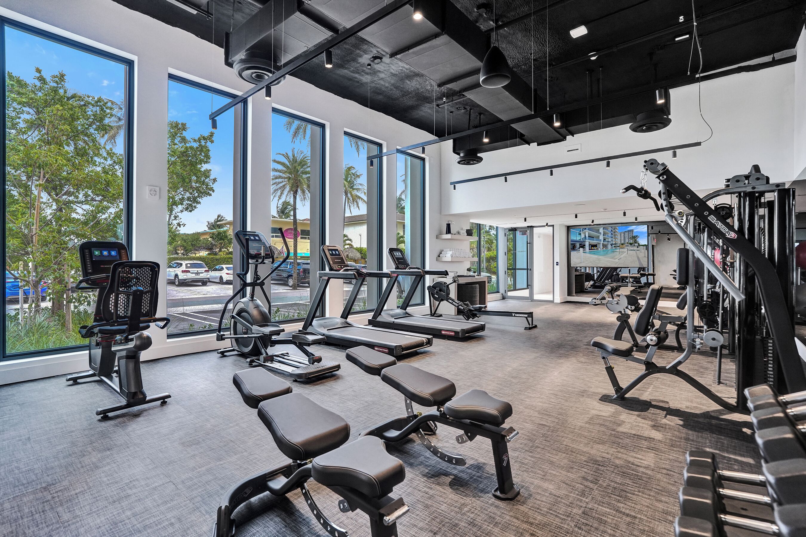 A gym with exercise equipment, large windows, and a view of the outside.