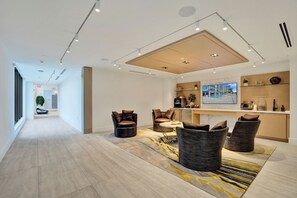 A spacious hotel lobby with a long corridor, seating area with chairs, a dining table, and a kitchen area with a large window. - Salato (Pompano Beach)