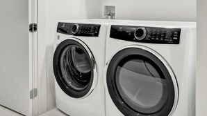 A modern laundry room with two front-loading washing machines, a white door, and a recessed ceiling light. - Salato (Pompano Beach)