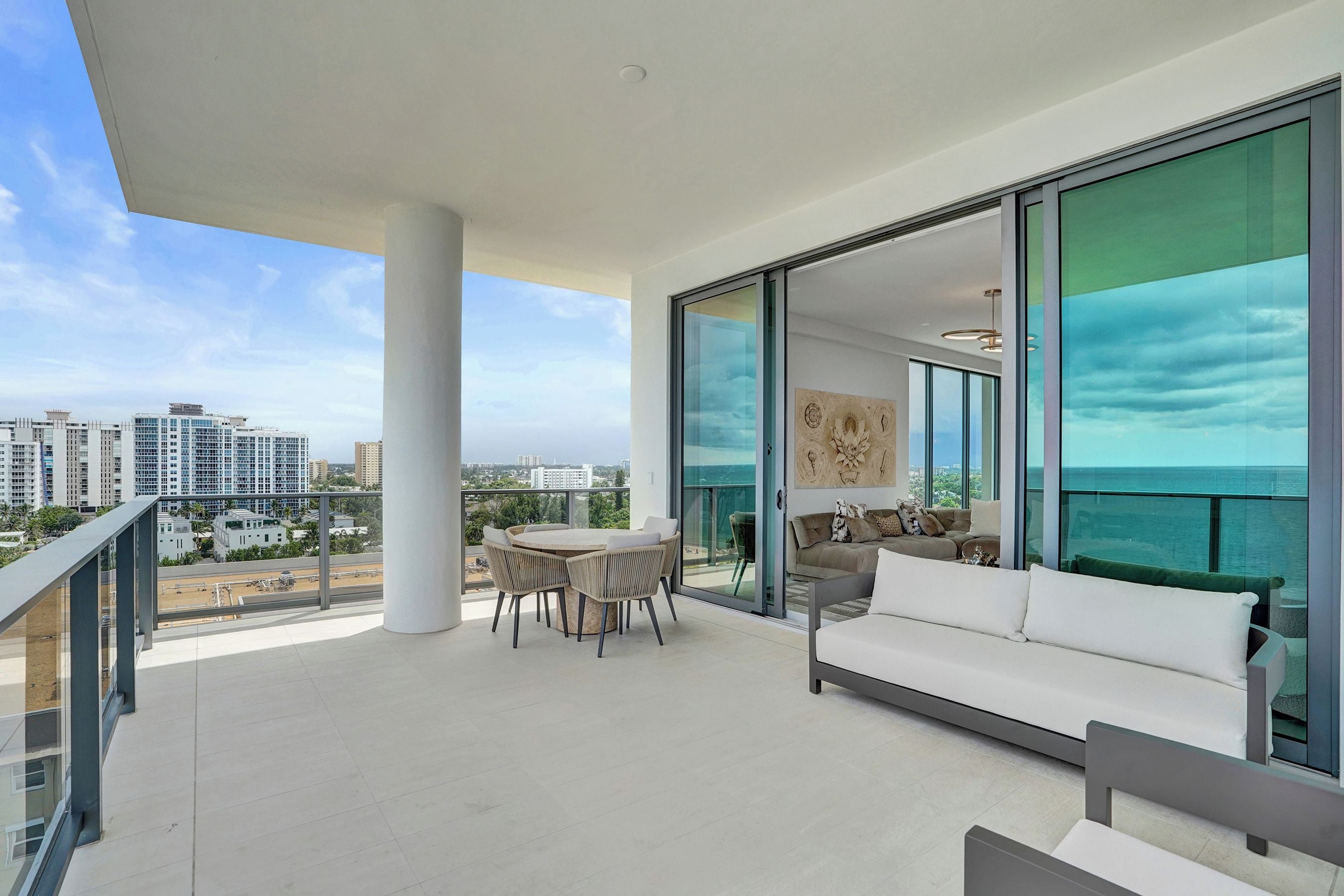 A spacious balcony with a dining area, a sofa, and a view of the cityscape.