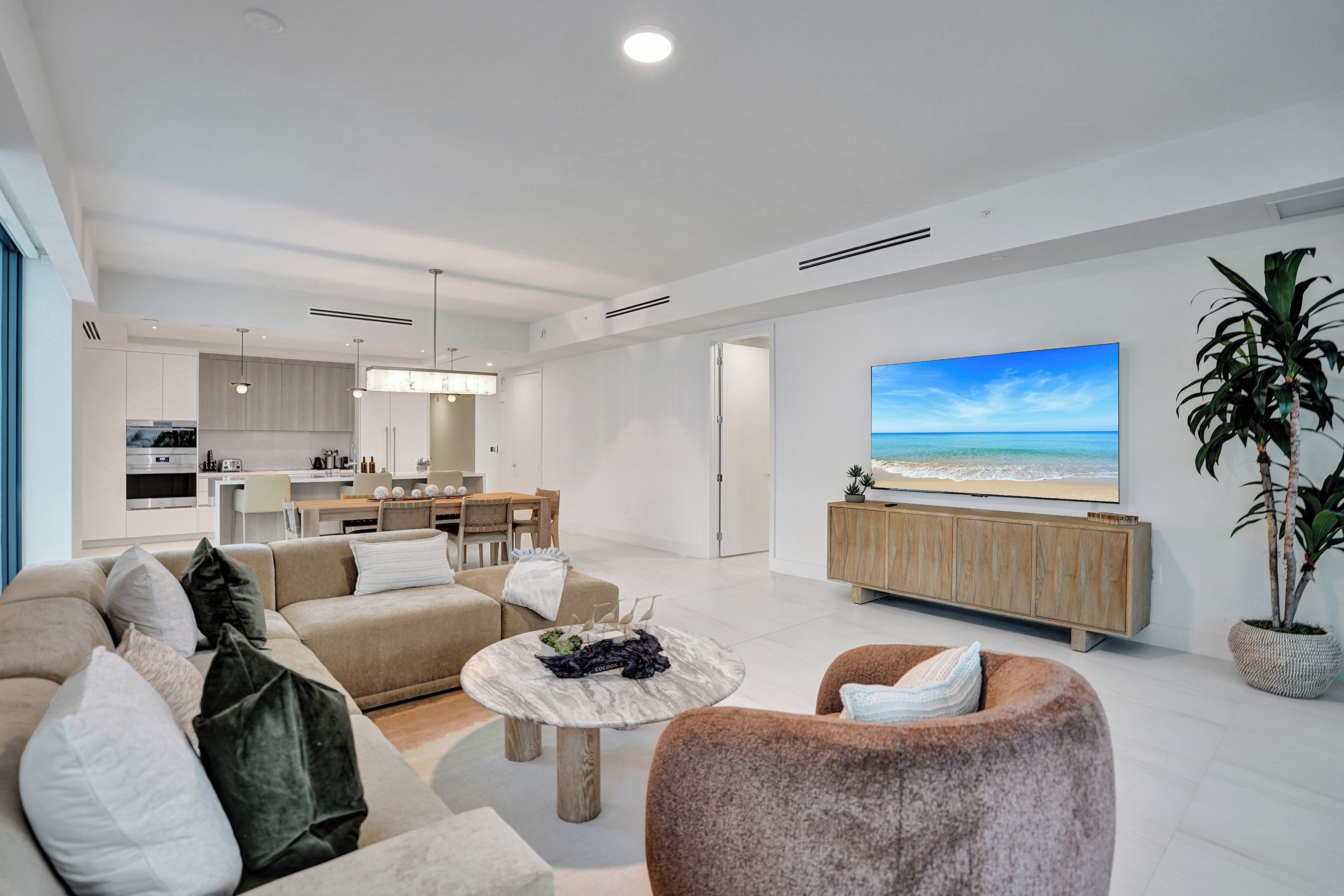 Een moderne woonkamer met een grote flatscreen televisie, een eethoek en een keuken.