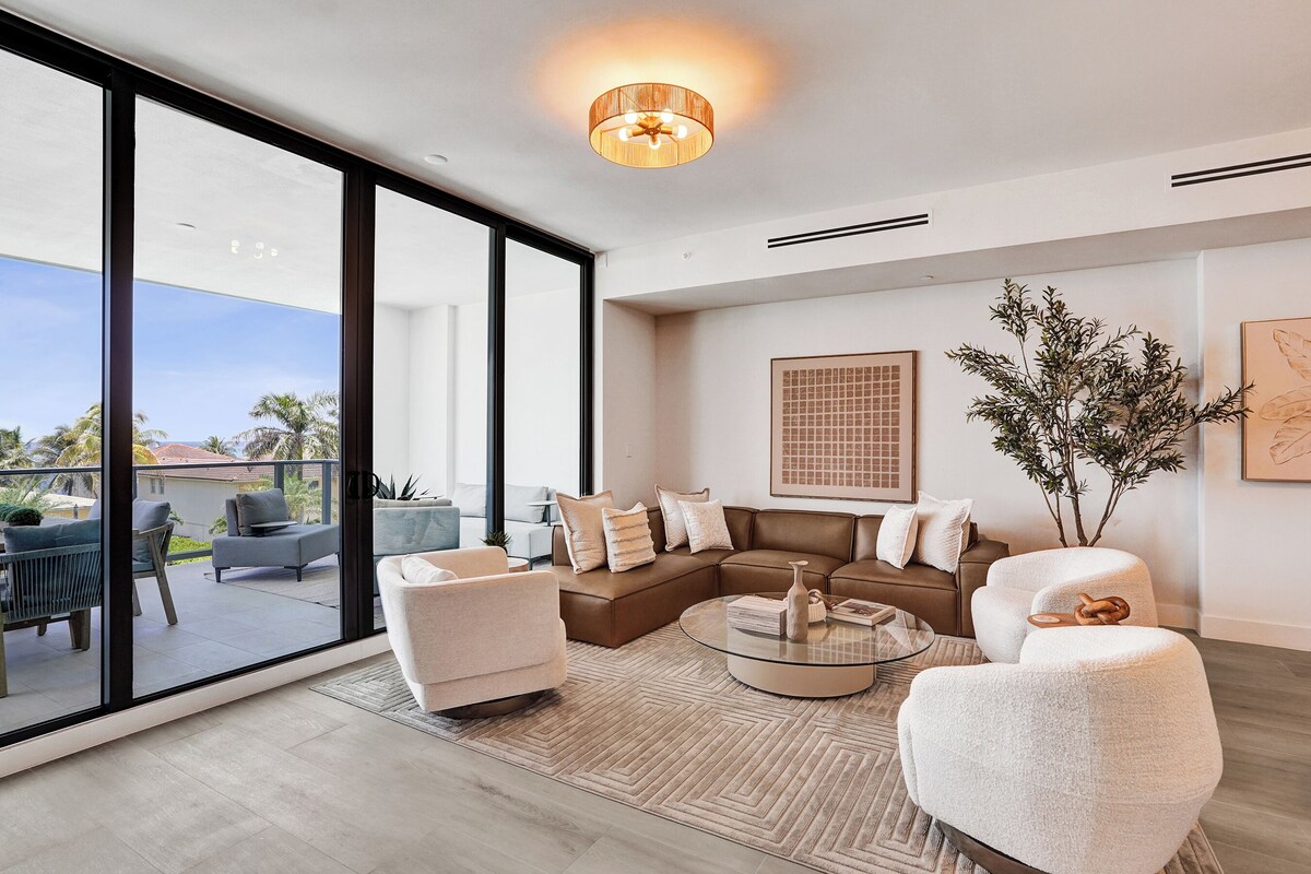 A modern living room with a sectional sofa, a coffee table, and a large window overlooking a balcony.
