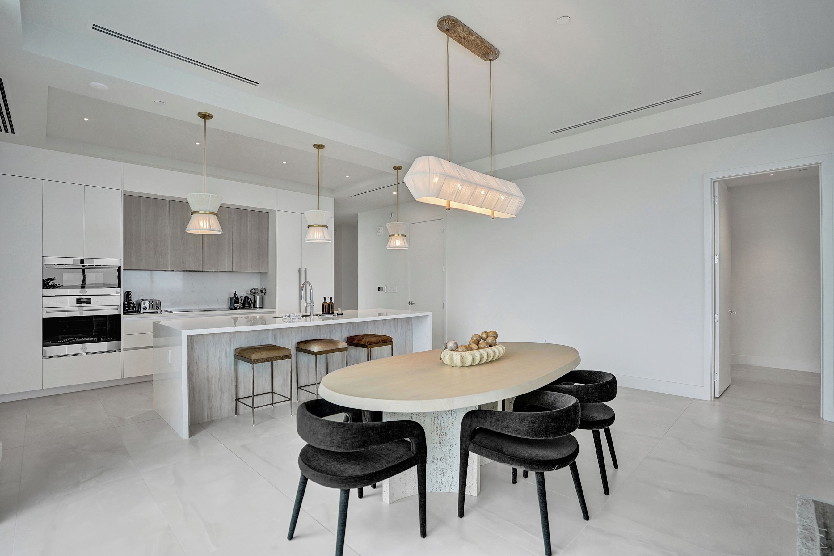 A modern kitchen with a central island, bar stools, pendant lighting, and a dining table with chairs.