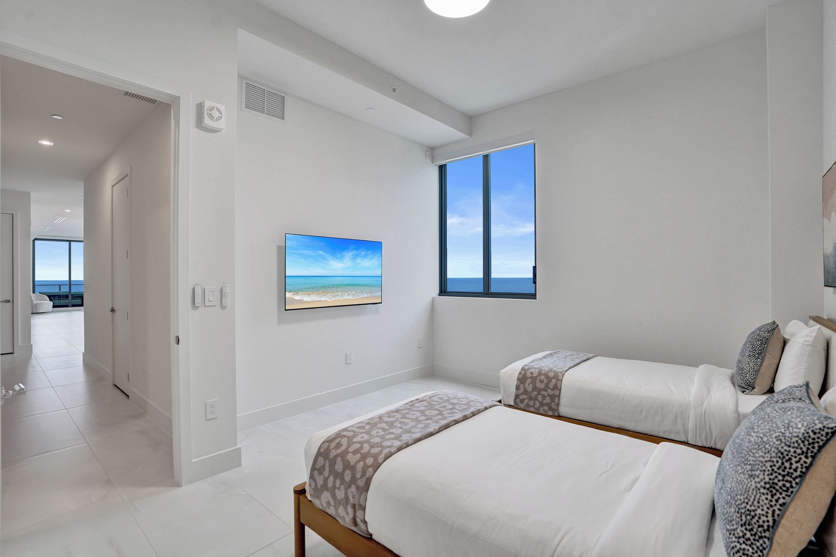A bedroom with two beds, a large window with a view, and a painting on the wall.