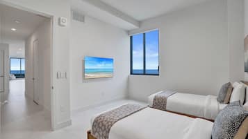 A bedroom with two beds, a large window with a view, and a painting on the wall.
