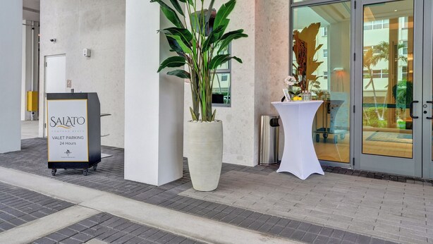 A valet parking sign, a large potted plant, and a glass door entrance to a building. - Salato (Pompano Beach)