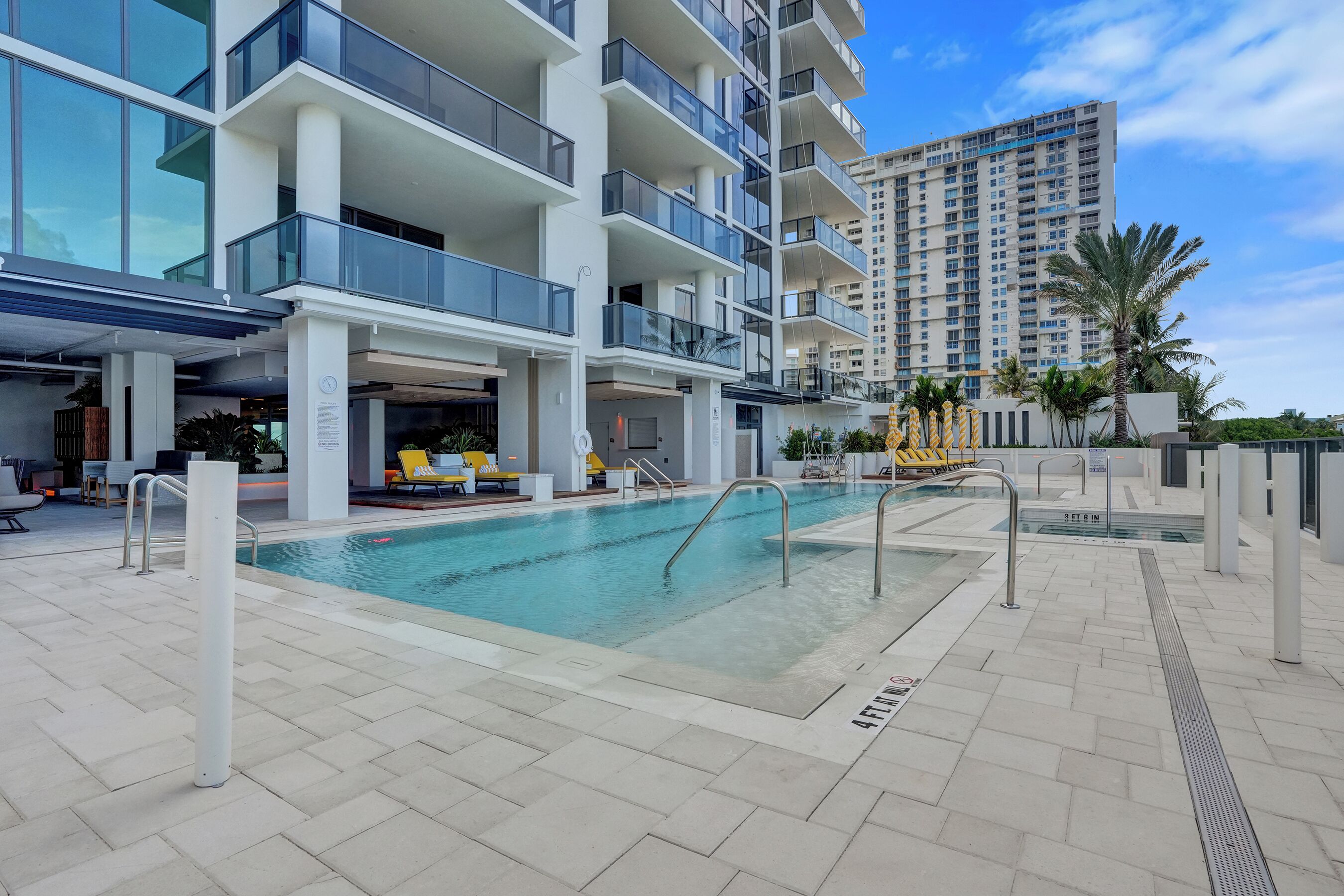 A modern hotel with a swimming pool, outdoor seating, and a view of a tall building.