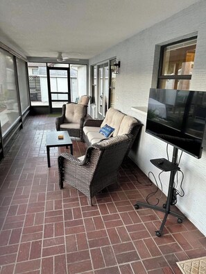 Un patio couvert aménagé avec des meubles en osier, un téléviseur à écran plat et un sol en briques.