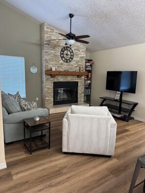 A living room with a fireplace, a sofa, a coffee table, a TV, and a bookshelf. - The Canal House on Lake Harris (Tavares)