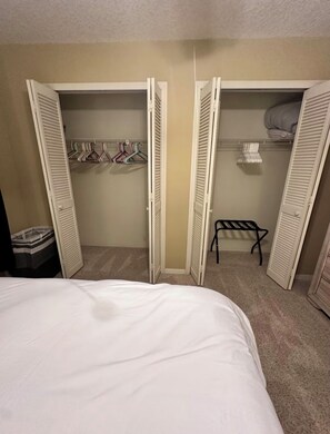 A bedroom with a bed, two open closets with hanging clothes, and a bench.