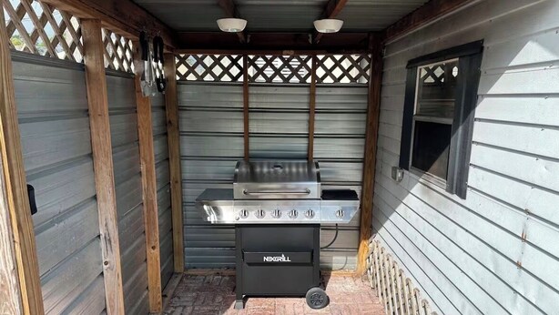 Ein Grill mit vier Kochfeldern und einem Seitenbrenner, platziert in einem überdachten Außenbereich mit Holzwabenverkleidung und einem Fenster auf der rechten Seite.