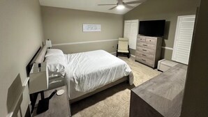 Ein Schlafzimmer mit Bett, Kommode, Fernseher und Deckenventilator.