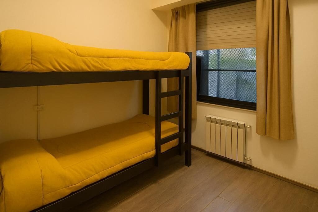 Una cama litera con ropa de cama amarilla en una habitación con ventana y radiador.