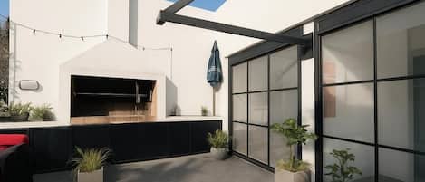 A modern outdoor kitchen area with a built-in oven, potted plants, and a large sliding glass door.