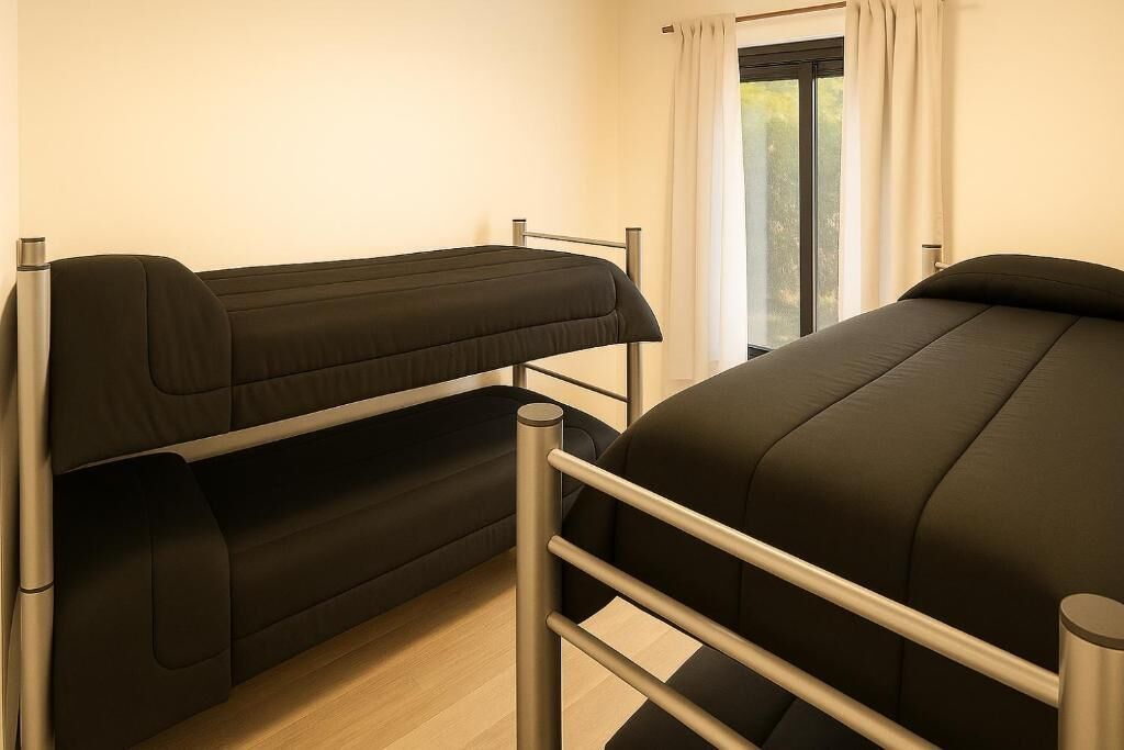 A room with two bunk beds, a window with curtains, and a view of greenery outside.