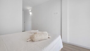 Quarto de hotel minimalista com uma cama grande, uma mesa de cabeceira e uma luminária fixada na parede.