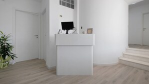 Um interior moderno com um balcão de recepção branco, uma planta em vaso e uma escadaria.