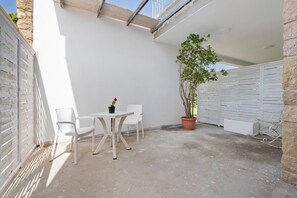 Un patio con una mesa, sillas, una planta en maceta y una pared blanca.
