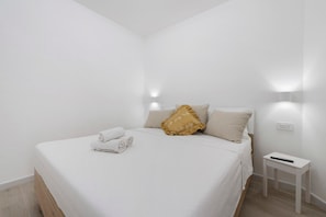 A minimalist bedroom with a bed, a bedside table, and a wall-mounted light. - Villa Matilde Domo Boutique - Stanza Chiara (Torre degli Ulivi)
