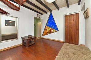 A room with wooden flooring, a door, a wall-mounted painting, a small table with a hat, and a mirror. - Villa  Luna LLena located in the Jamanota hills of Aruba's Arikok National park (Santa Cruz)