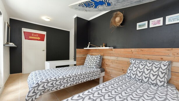 A room with two beds, a white desk, a black wall with framed pictures, and an exit sign. - Villa  Luna LLena located in the Jamanota hills of Aruba's Arikok National park (Santa Cruz)