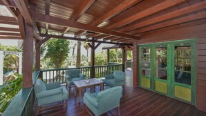A covered outdoor area with wooden flooring, green-framed glass doors, and light blue upholstered chairs. - Villa  Luna LLena located in the Jamanota hills of Aruba's Arikok National park (Santa Cruz)