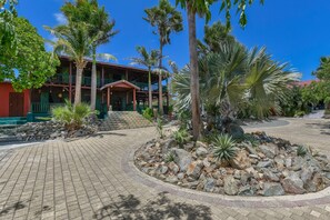 A resort with a paved walkway, palm trees, and a building with a red facade. - Villa  Luna LLena located in the Jamanota hills of Aruba's Arikok National park (Santa Cruz)