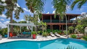 A pool area with a covered seating area, lounge chairs, and a two-story building with balconies. - Villa  Luna LLena located in the Jamanota hills of Aruba's Arikok National park (Santa Cruz)