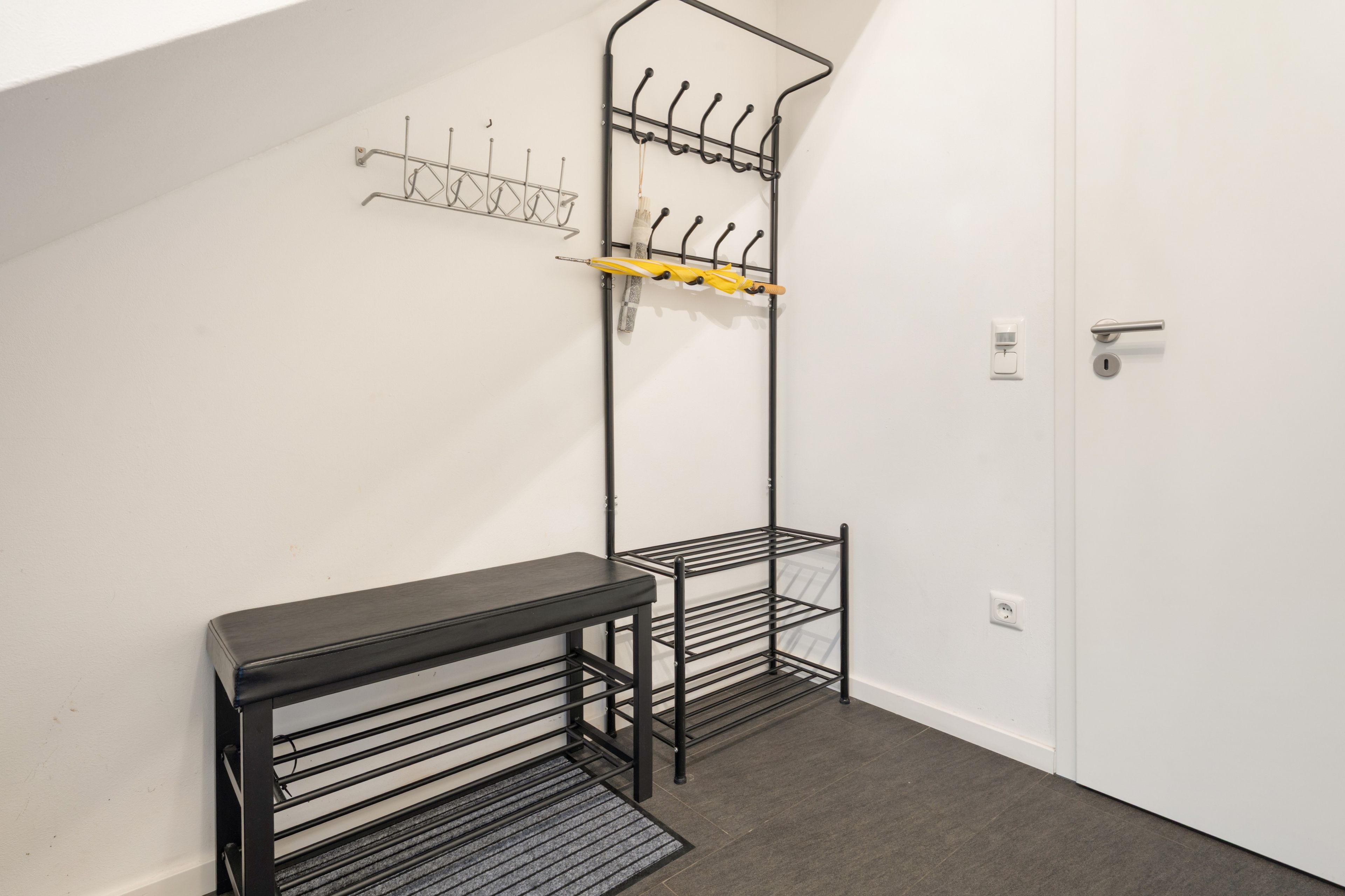 A hallway with a coat rack, a bench, and a door.