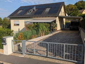 A house with a sloped roof, solar panels, a covered porch, and a gated driveway. - Apartment 'Malbrich' with Private Terrace and Wi-Fi (Gräfenberg)