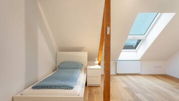 Una habitación pequeña y luminosa con una cama individual, una mesita de noche y un tragaluz.