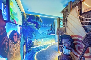 Een kamer met een muurschildering van een tropisch strand, een groot decoratief zeil en een beeld van een personage.