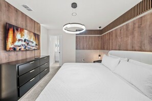 Een moderne slaapkamer met een groot bed, een dressoir, een flatscreen televisie en een plafondlamp.