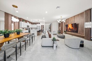 A modern kitchen with white cabinets, a dining area with a wooden table and grey chairs, and a living room with a grey sofa and a flat-screen TV. - 8BR house at Windsor Cay Resort (Clermont)