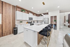 A modern kitchen with white cabinetry, a central island with bar stools, and a stainless steel refrigerator. - 8BR house at Windsor Cay Resort (Clermont)