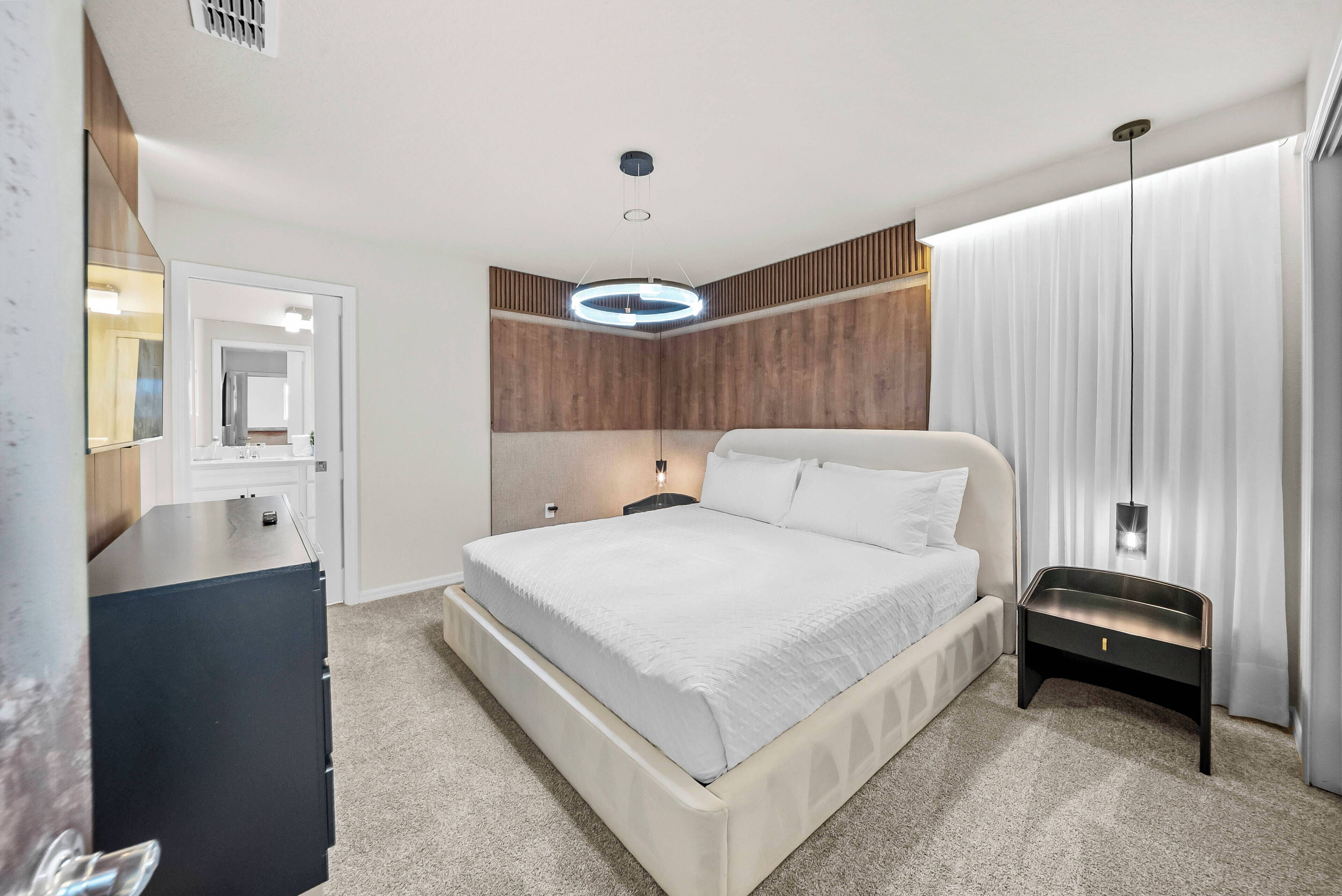 A modern hotel room with a large bed, a bedside table, a dresser, and a mirror.