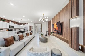 A modern living room with a sofa, coffee table, and a flat-screen TV mounted on a wooden wall. - 8BR house at Windsor Cay Resort (Clermont)
